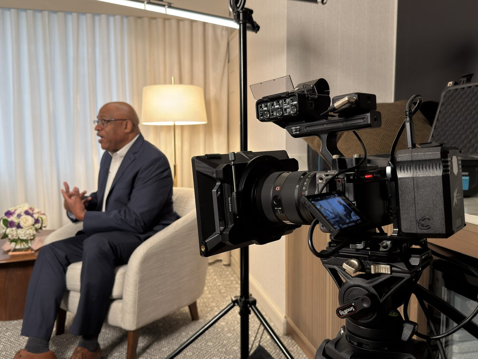 Close-up of a cinema camera rig with an interview subject in soft focus behind it