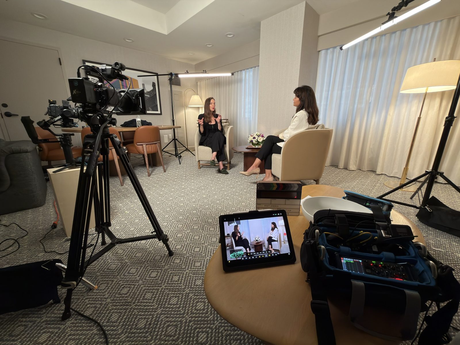 Wide shot of a two-person interview setup with camera, monitor, and audio bag in frame